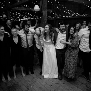 Bride and guests sharing joyful embrace under string lights at rustic barn wedding in Maine.