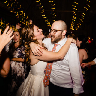 Bride and groom dancing joyfully at Cunningham Farm wedding surrounded by guests and glowing string lights.