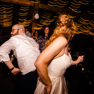 Bride and groom dancing joyfully under warm string lights at a rustic Maine barn wedding.