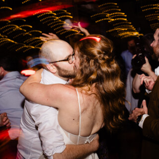 Bride and groom share a passionate kiss on a vibrant wedding dance floor.