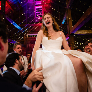 Bride laughing mid-Horah dance at rustic barn wedding in New Gloucester, Maine.