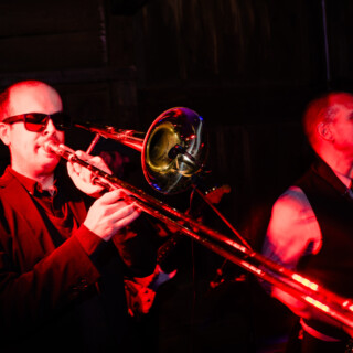 Trombonist and saxophonist performing live under red stage lights at a jazz club.