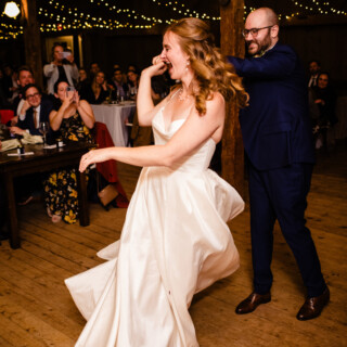 Bride and groom share joyful first dance at rustic barn wedding under warm string lights.