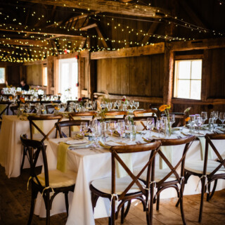 Rustic barn wedding reception with elegant tables, white linens, green accents, and glowing fairy lights.