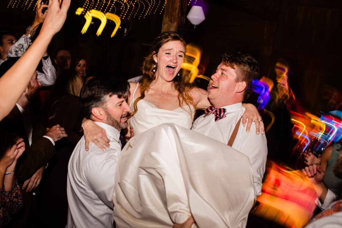 Bride lifted joyfully on dance floor during lively Cunningham Farm wedding celebration in Maine.