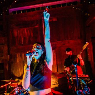 Female singer performing with live band under colorful lights at rustic barn wedding in Maine.