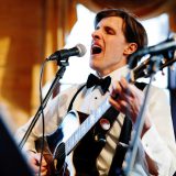 Emotional wedding singer performing live with acoustic guitar under warm golden light.