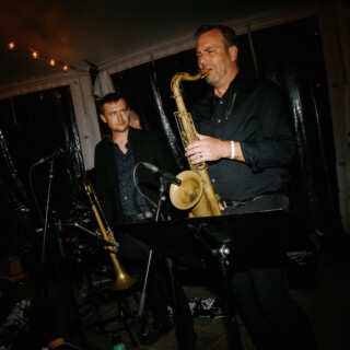 Two jazz musicians performing under warm string lights at an intimate evening event in Beverly, MA.