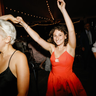 Two women dancing joyfully under warm string lights at a Moraine Farm wedding reception.