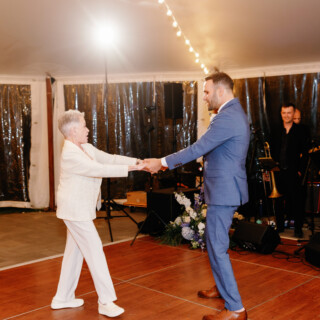 Grandmother and grandson dancing joyfully under string lights at an elegant Moraine Farm wedding.