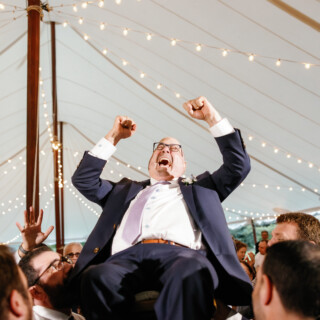 Groom lifted in joyous hora dance under glowing lights at Moraine Farm wedding.