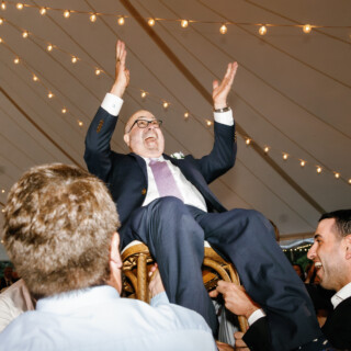 Groom lifted on a chair during joyful Moraine Farm wedding celebration under glowing string lights.