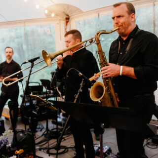 Live jazz trio performing under a glowing tent at an elegant outdoor wedding in Beverly.