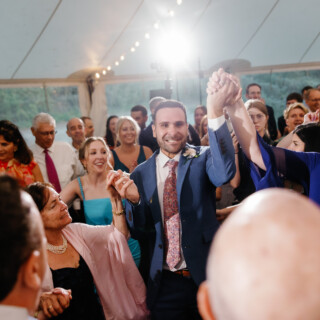 Groom dancing joyfully with guests under string lights at Moraine Farm wedding in Beverly, MA.