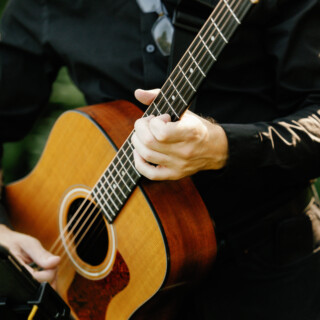 Musician playing acoustic guitar outdoors in warm sunlight with natural wood tones and soft focus.