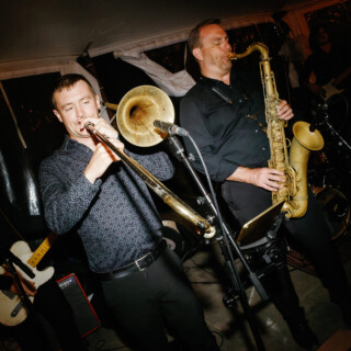 Live jazz band performing on stage with trombone, saxophone, guitar, and warm golden lighting