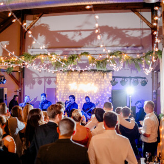 Lively indoor wedding reception with live band, string lights, and joyful guests in Vermont.