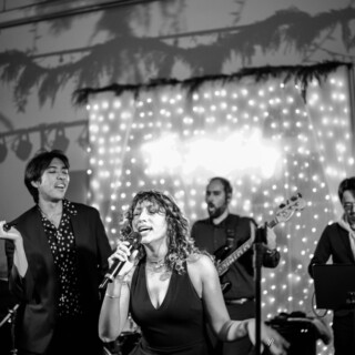 Emotional black-and-white live performance with passionate vocal duo and glowing string lights backdrop.