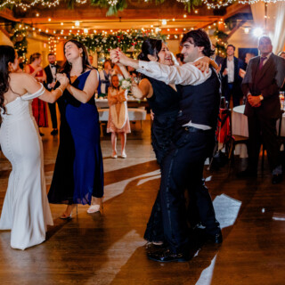 Bride and groom dancing at rustic Vermont wedding under warm string lights and greenery.