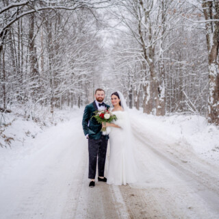 Bride and groom on snowy forest road at romantic winter wedding in Vermont.