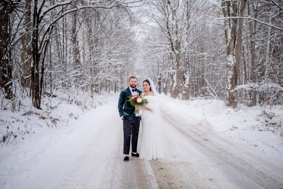 Bride and groom on snowy forest road at romantic winter wedding in Vermont.