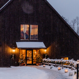 Snow-covered wooden lodge glowing with warm holiday lights on a peaceful winter evening.