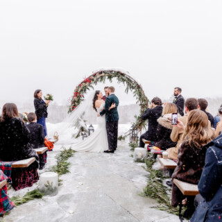 Bride and groom kiss under snowy evergreen arch at Mountain Top Inn winter wedding in Vermont.