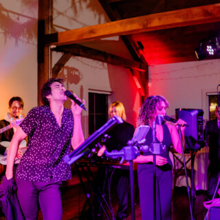 Live band performing at rustic indoor wedding venue with colorful lights and energetic singers.