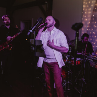 Emotional live band performance with passionate singer, saxophonist, and drummer under warm purple lighting.