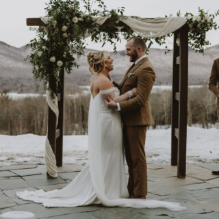 Bride and groom exchanging vows under floral arch at snowy mountain wedding in Vermont.