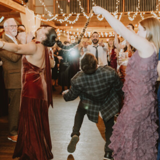 Guests cheer during a lively limbo dance at a rustic Vermont barn wedding reception.