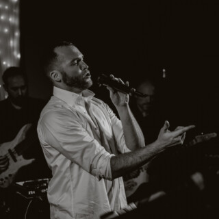 Black and white photo of emotional live singer performing with band under soft twinkling lights.