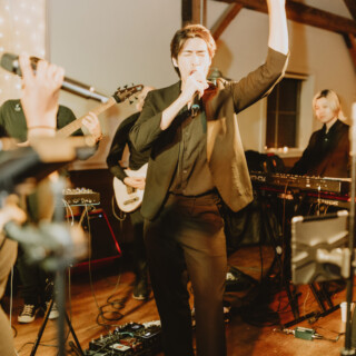 Passionate lead singer performing with live band on warm-lit indoor stage during intimate concert.