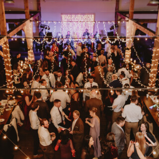 Rustic barn wedding reception with guests dancing under warm string lights and wooden beams.