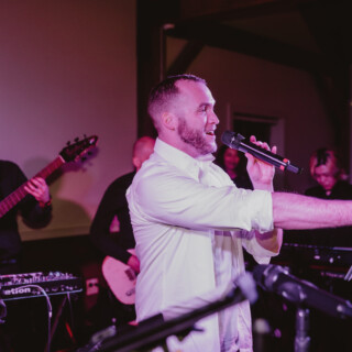 Singer performing with live band under warm string lights at cozy indoor wedding venue.