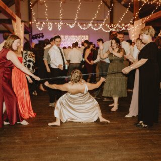 Bride limbo dancing under fairy lights at a rustic Vermont wedding reception.