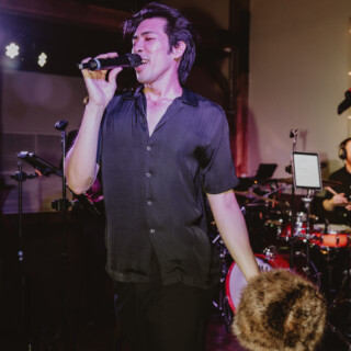 Male singer performing passionately on stage under colorful lights with live band in vibrant atmosphere.