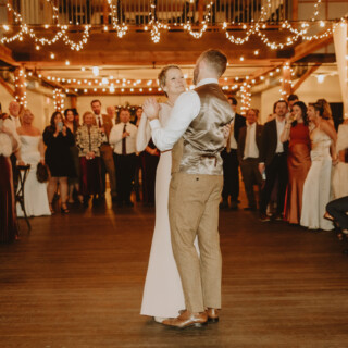 Bride and groom share first dance under string lights at rustic barn wedding in Vermont.