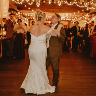 Bride and father share emotional dance under glowing string lights at rustic Vermont wedding reception.