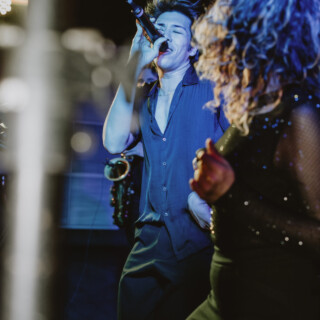 Male singer performing passionately with energetic female dancer under vibrant blue and purple stage lights.
