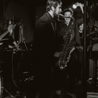 Black-and-white jazz performance with passionate saxophonist and lively audience in intimate music venue.